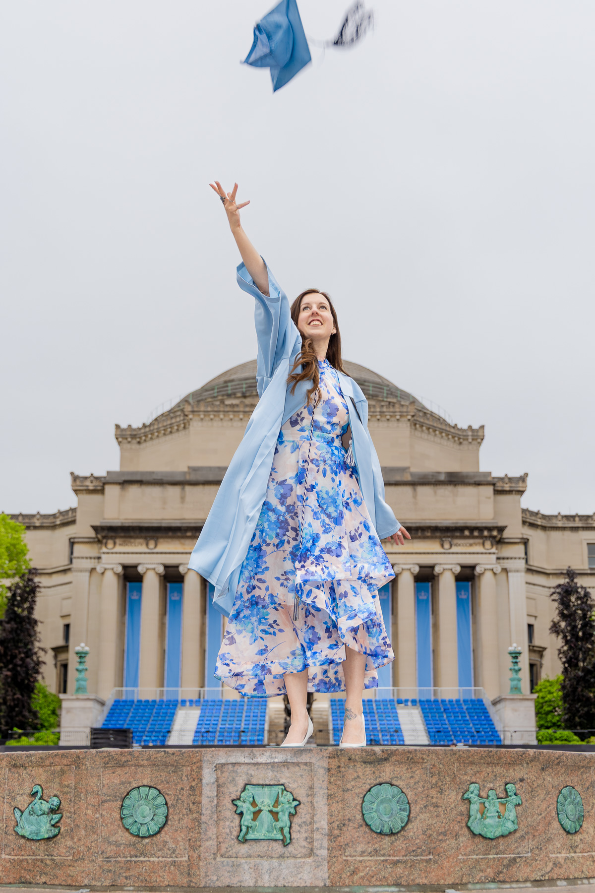 grad student celebrating and tossing her cap on campus